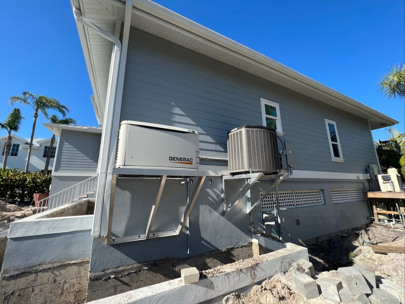 Generac standby generator and AC condenser mounted on elevated aluminum platforms above flood level at a coastal Tampa Bay stilt home by Lightning Bay Electric