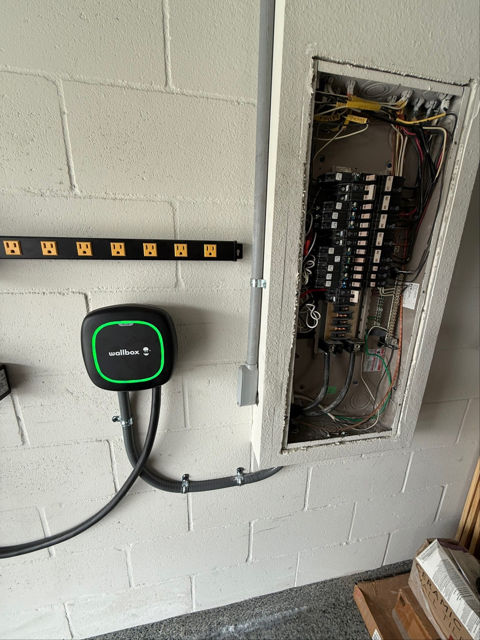 Wallbox Pulsar Plus EV charger installed beside the electrical panel in a block garage by Lightning Bay Electric in the Tampa Bay area